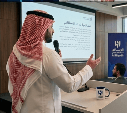 رجل بالزي السعودي يقدم عرضاً عن استراتيجية الذكاء الاصطناعي ممسكاً بميكروفون أمام شاشة عرض.